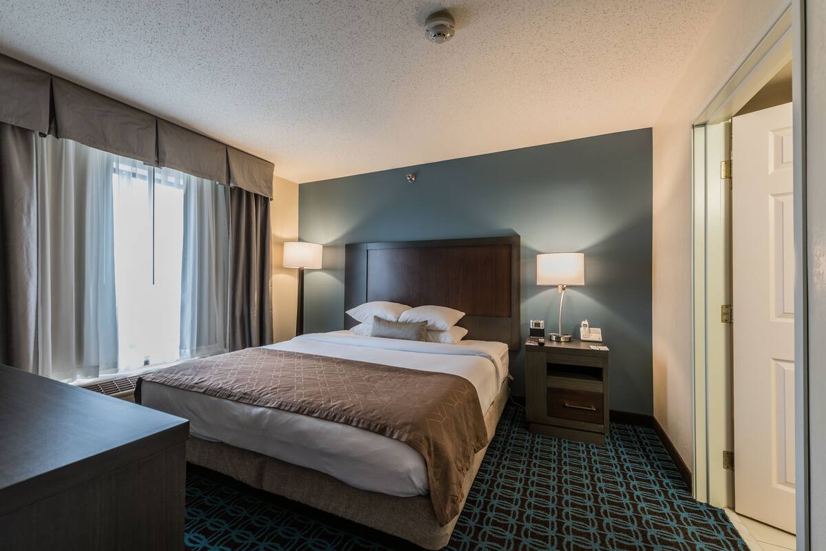 A hotel room with a bed, bedside lamps, a desk, and a patterned carpet.