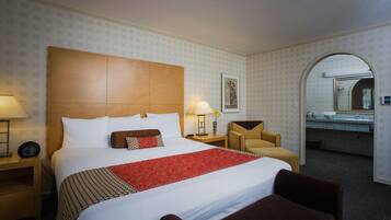 A hotel room with a large bed, two bedside tables, a chair, a desk, and a bathroom visible through an archway.