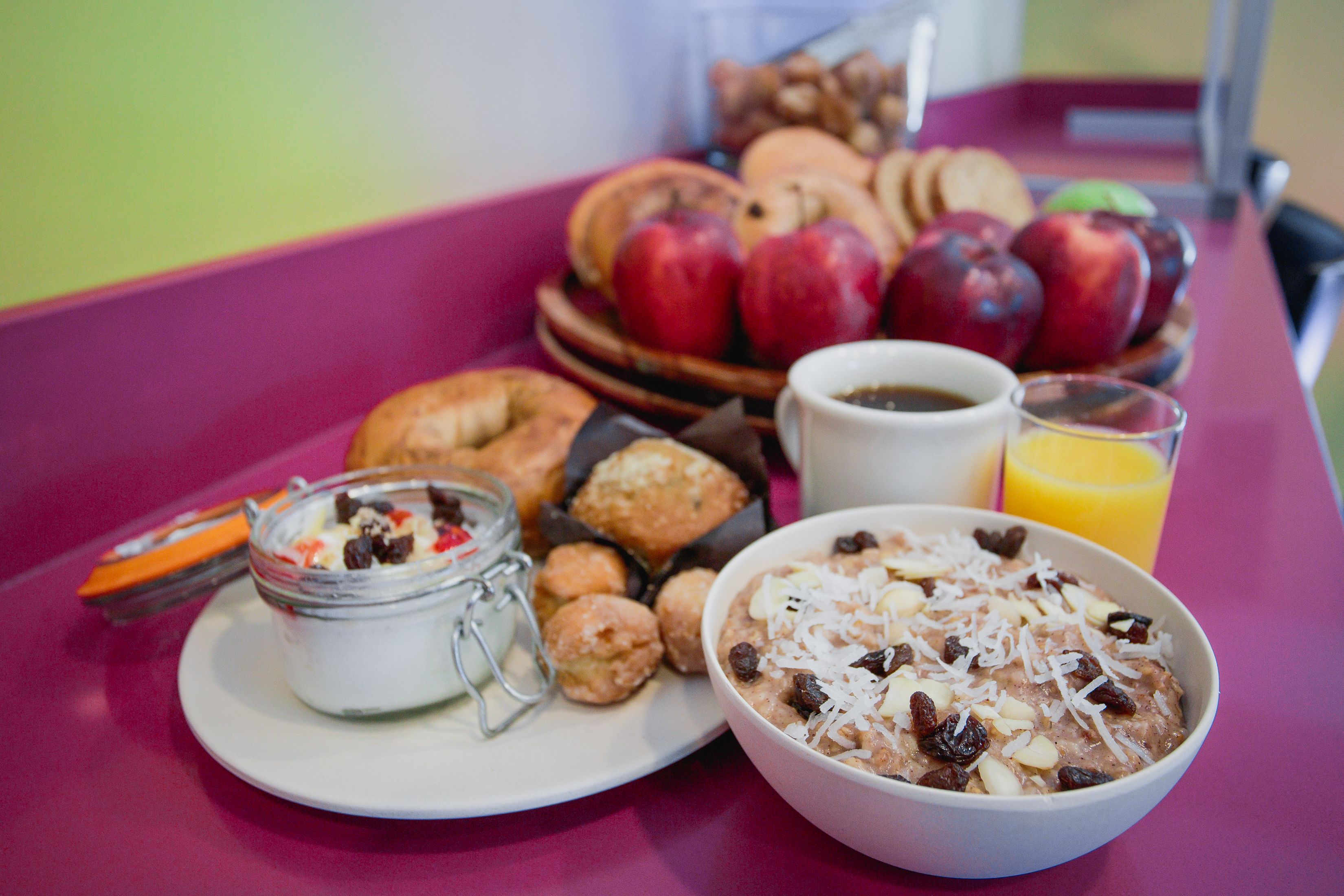 A breakfast table with a bowl of oatmeal, a plate of pastries, a jar of yogurt, and a plate of fruit.