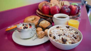 A breakfast table with a bowl of oatmeal, a plate of pastries, a jar of yogurt, and a plate of fruit.