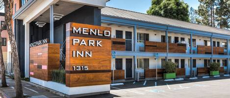 Edificio moderno del Menlo Park Inn con un cartel llamativo, estacionamiento y entrada cubierta.
