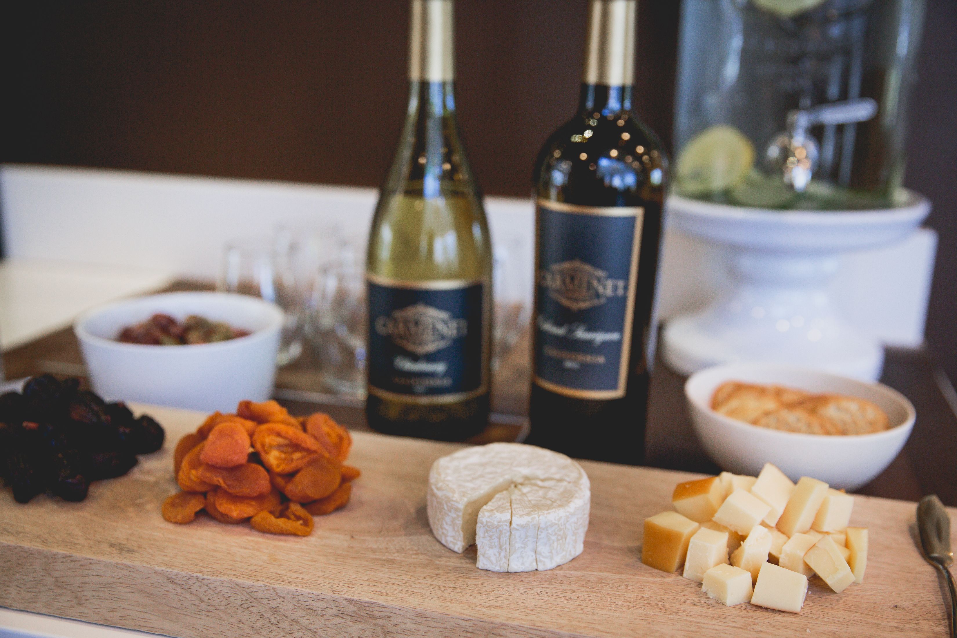 A wooden board with various cheeses, dried fruits, and two bottles of wine.