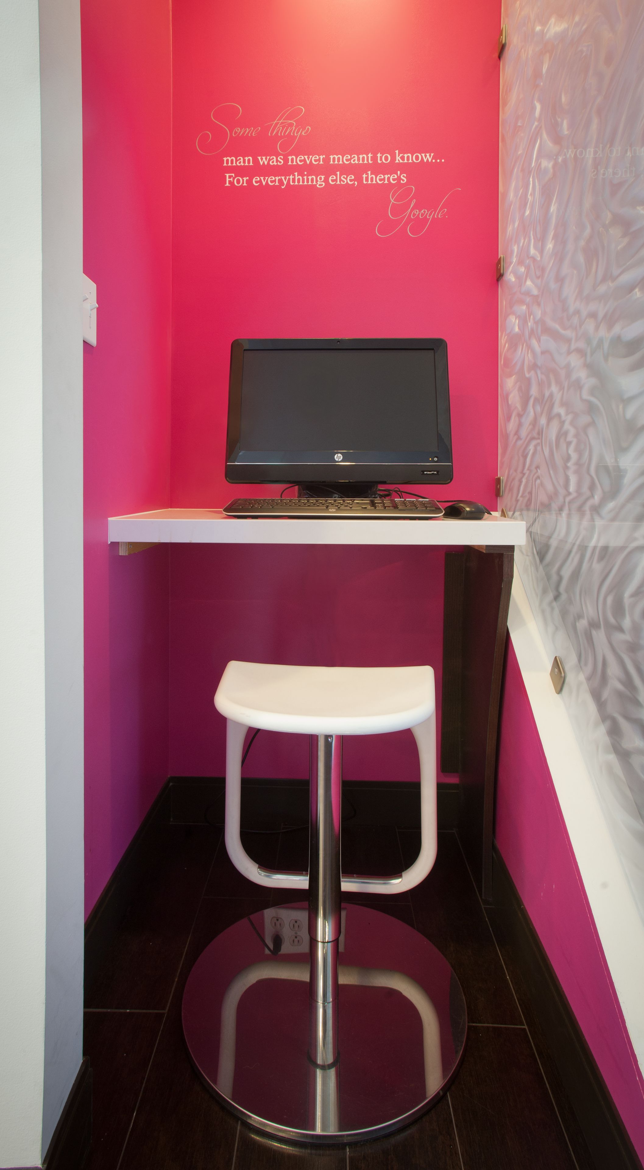 A small, brightly colored room with a pink wall, a white stool, and a desk with a laptop.
