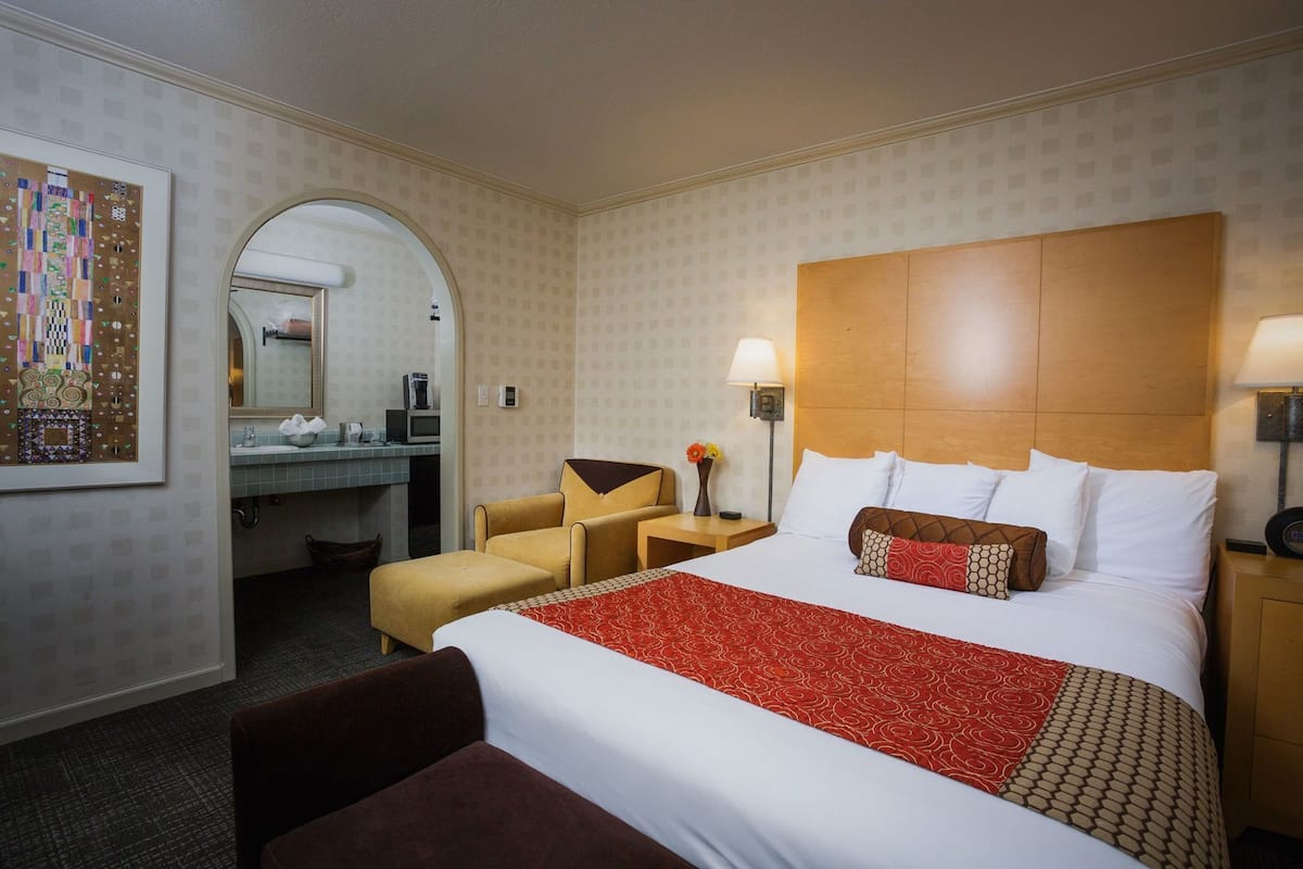 Hotellihuone, jossa on suuri sänky, peilillä varustettu työpöytä, tuoli ja pieni lamppupöytä.