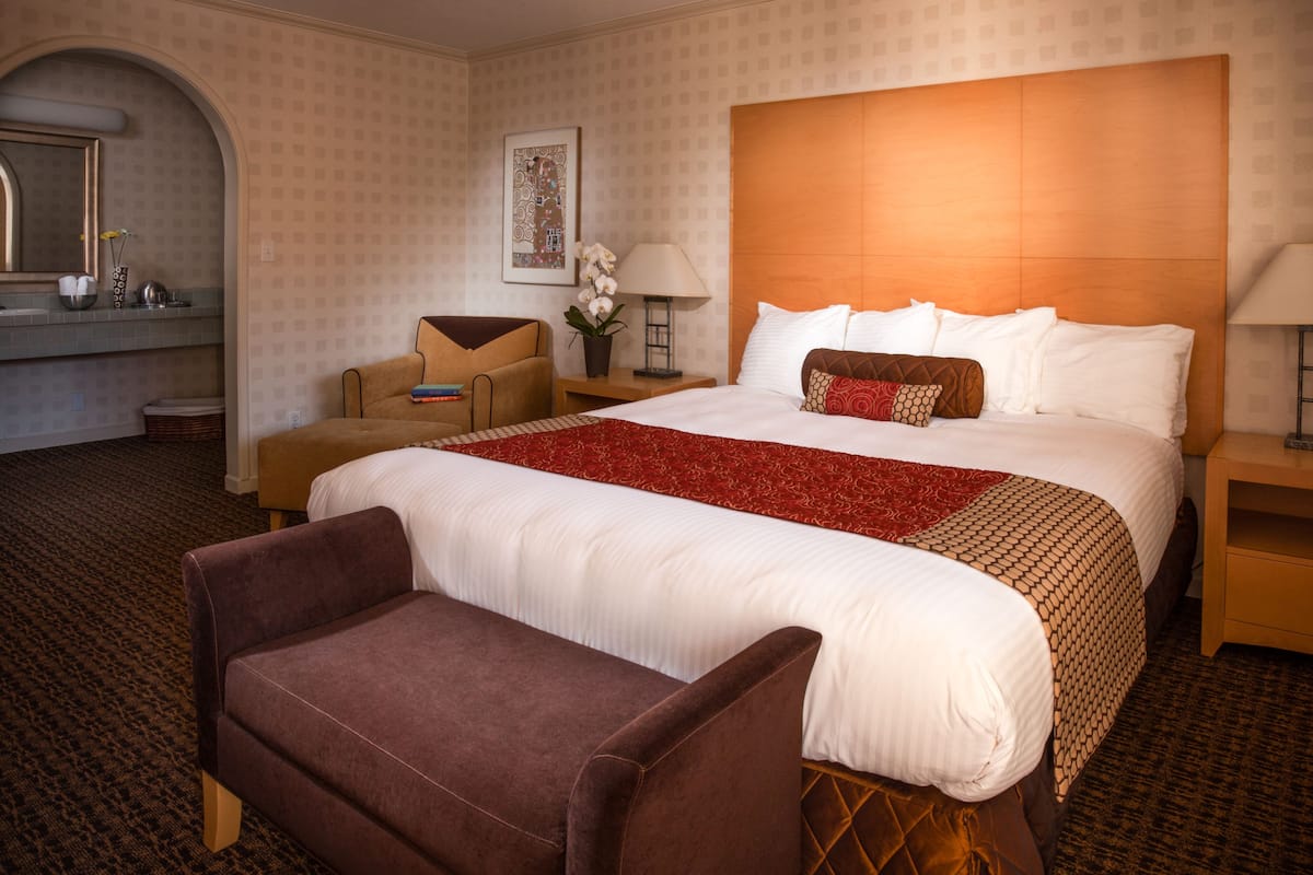 Hotellihuone, jossa on suuri sänky, oleskelualue, jossa on tuoli ja pieni pöytä, yöpöytä ja peili.