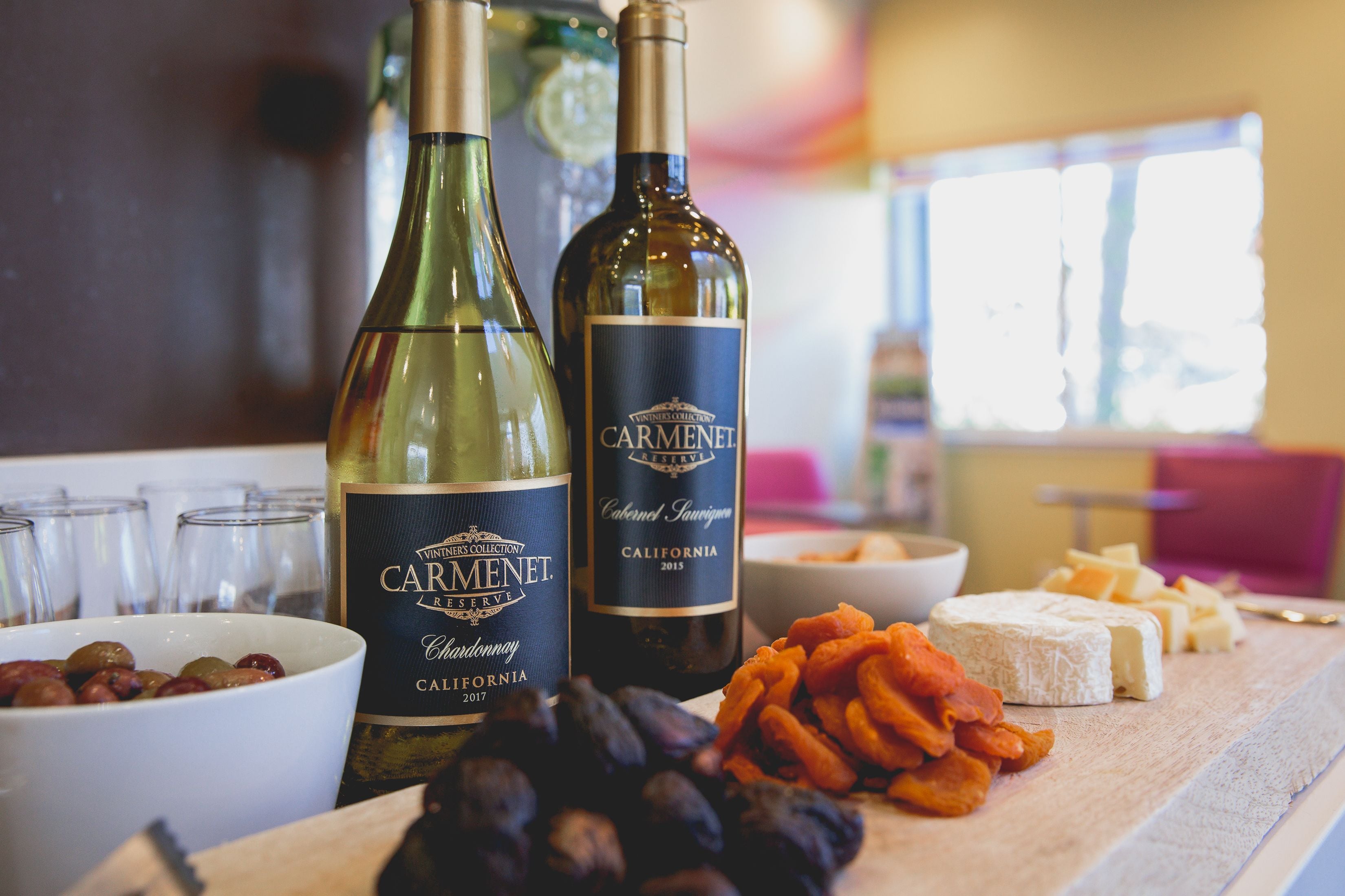 A table with wine bottles, cheese, and grapes.