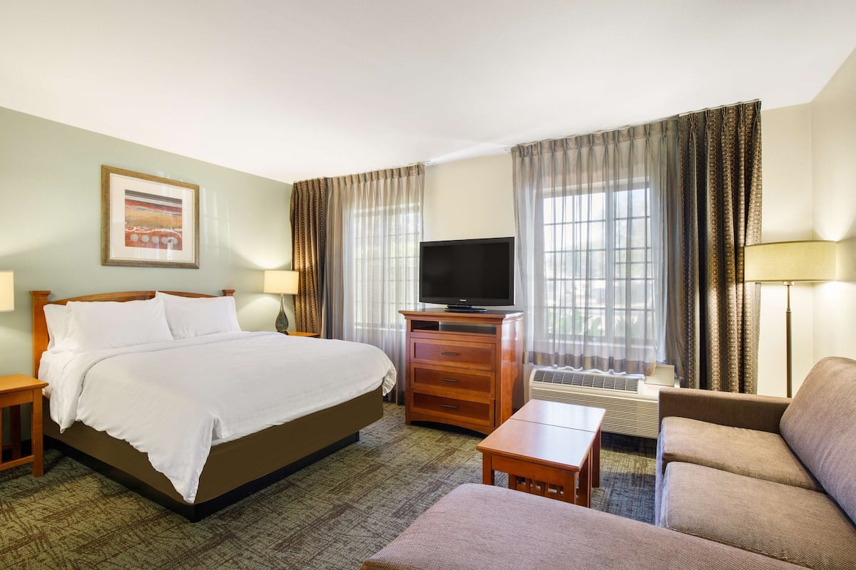 A hotel room with a bed, a television, a desk, a chair, and a window with curtains.