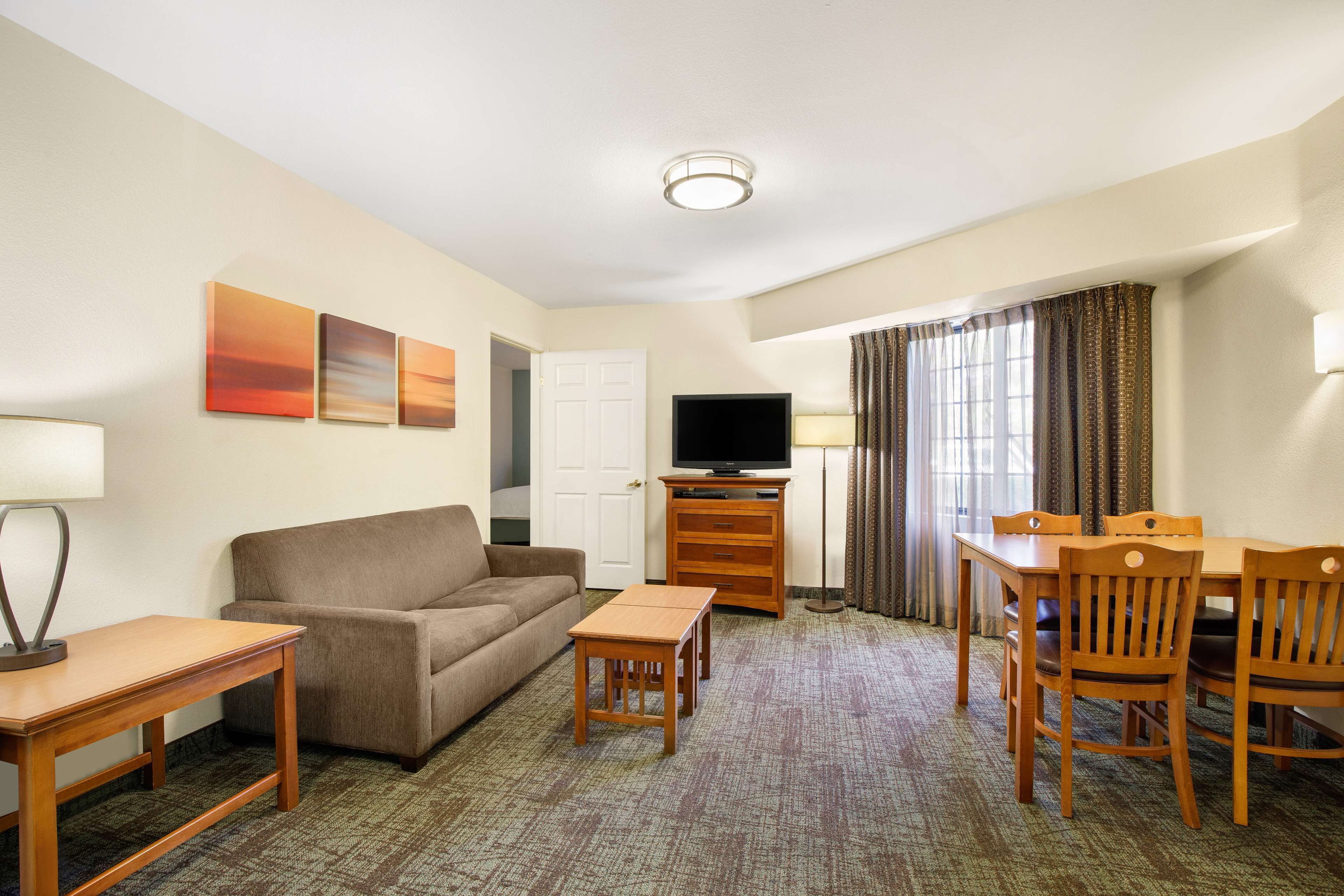 Ein Hotelzimmer mit einer Couch, einem kleinen Tisch, einem Fernseher auf einem Standfuß, einem Esstisch mit Stühlen und einem gemusterten Teppich.