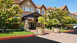 A multi-story hotel with a stone facade, a covered entrance, and landscaped gardens. - Sonesta ES Suites San Diego - Rancho Bernardo (San Diego)