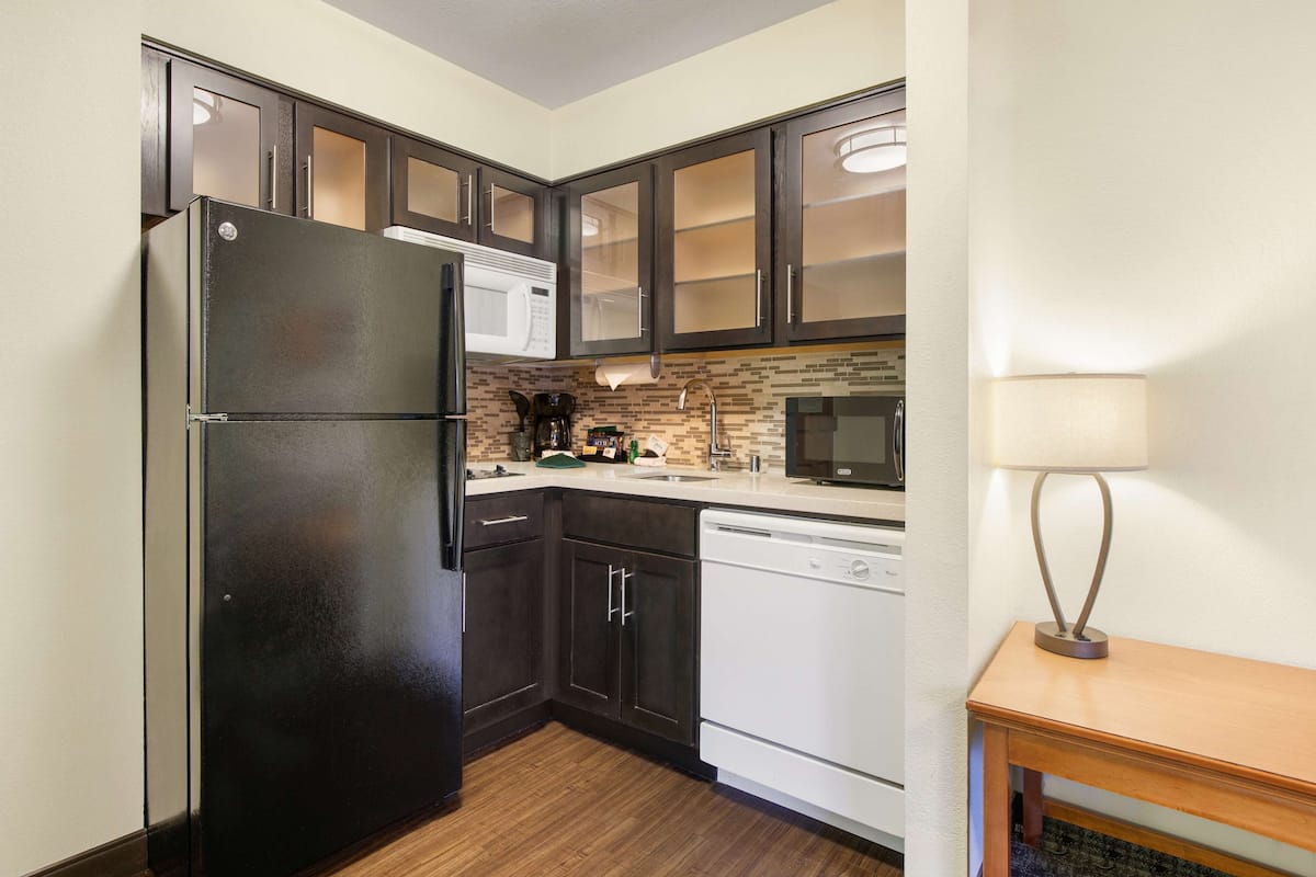 A compact kitchen with dark cabinets, a black refrigerator, a white dishwasher, and a microwave.