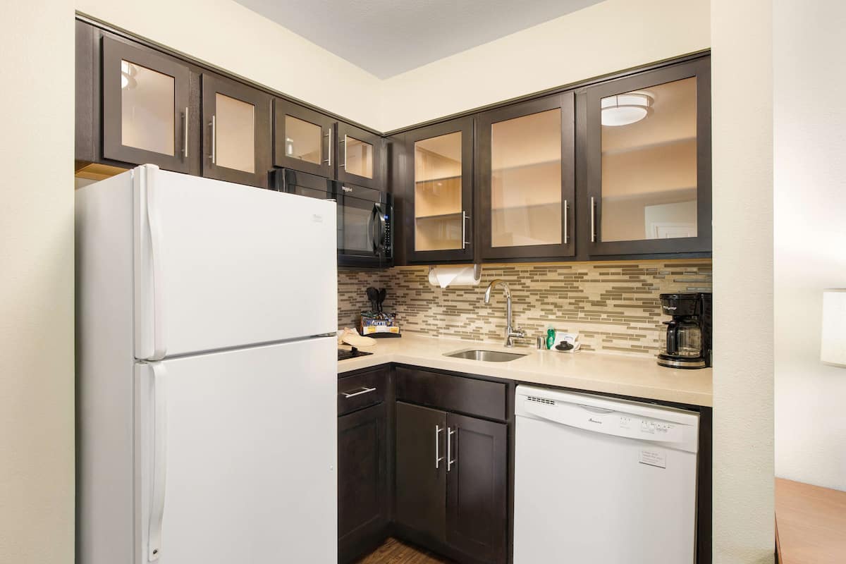 A compact kitchen with dark cabinets, a white refrigerator, a microwave, a coffee maker, and a dishwasher.