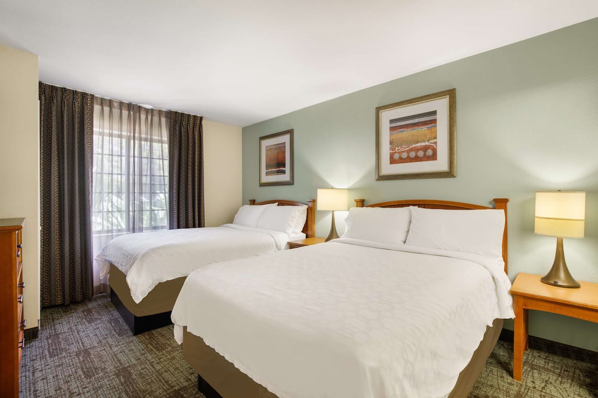 A hotel room with two beds, a dresser, two bedside tables with lamps, and two framed pictures on the wall.