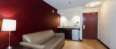 Un espacio habitable compacto con sofá, una mesita, kitchenette y una puerta.