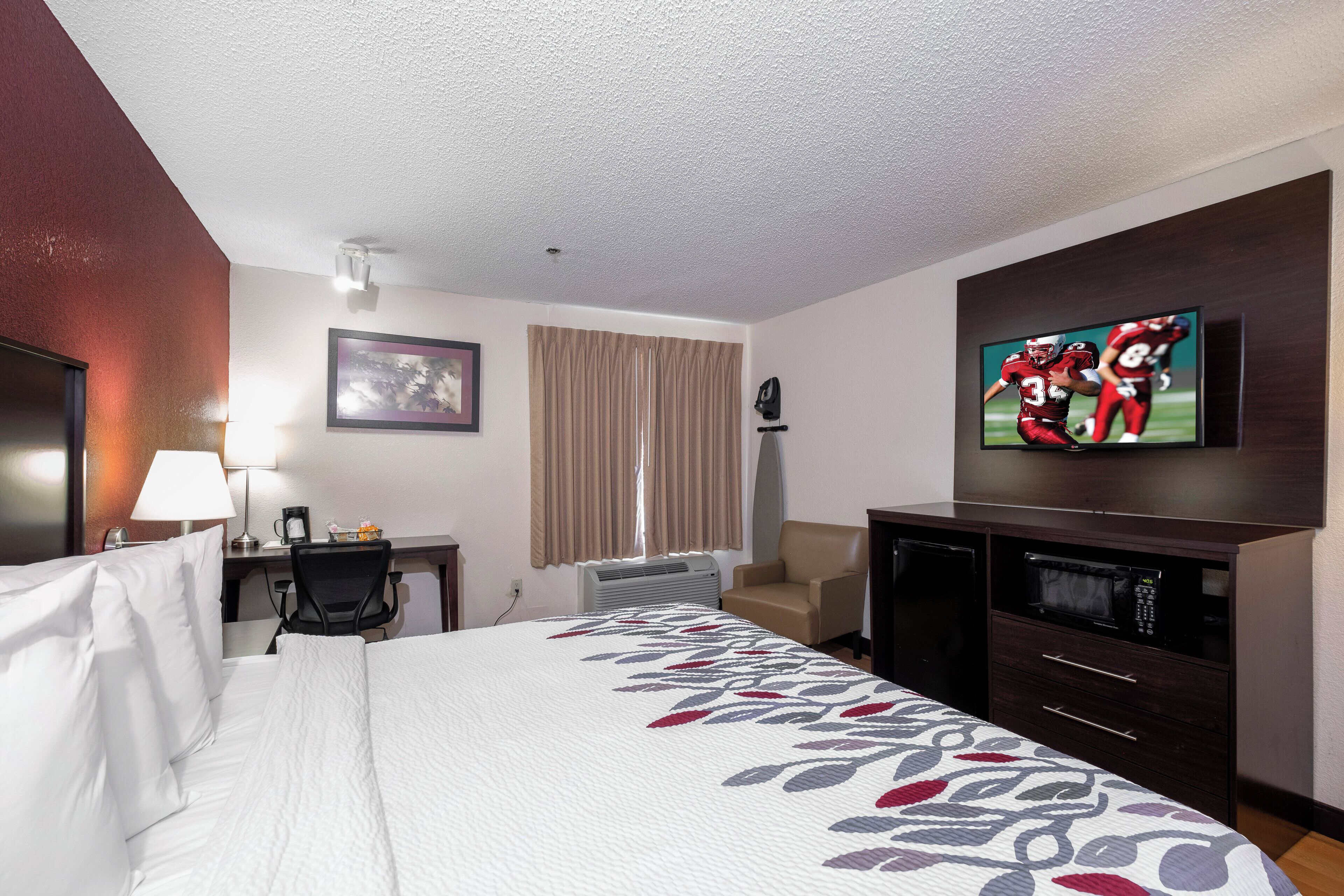 A hotel room with a bed, a desk, a chair, a television, and a window with curtains.