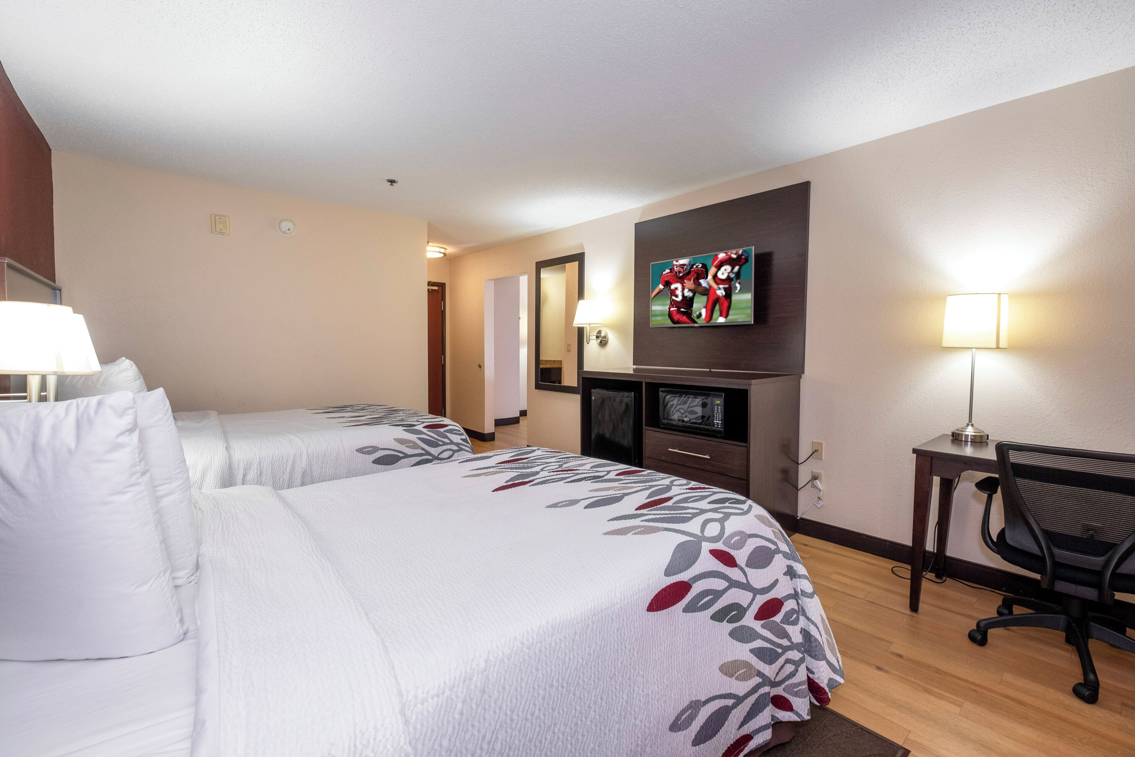 A hotel room with two beds, a desk, a chair, a television, and a microwave.