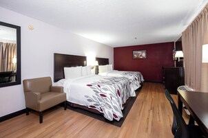 Una habitación de hotel con cama, una silla, un escritorio y un cuadro en la pared.