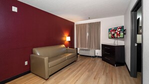 A room with a red wall, a beige sofa, a TV on the wall, and a heater on the floor. - Red Roof Inn & Suites Dover Downtown (Dover)
