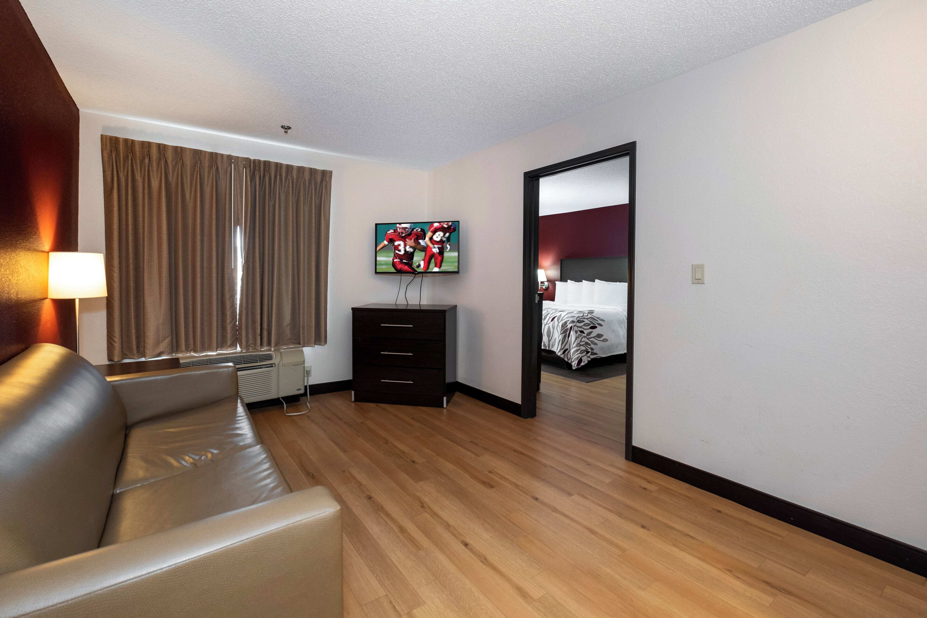 A hotel room with a sofa, a TV, a dresser, and a bed.