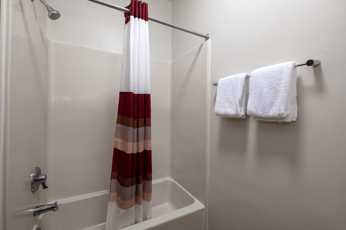 A bathroom with a shower curtain, a bathtub, and two white towels hanging on a wall.