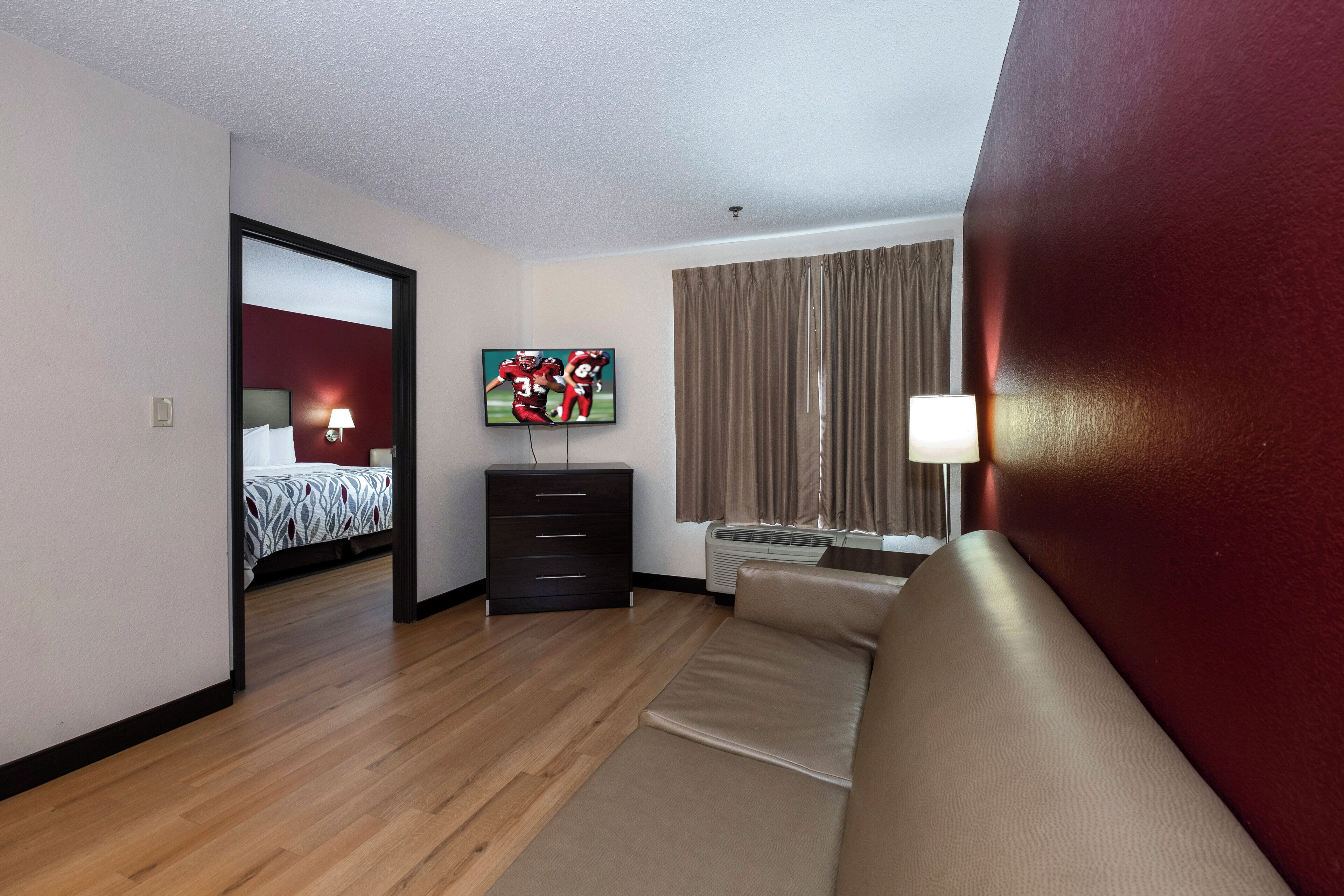 Una habitación de hotel con cama, televisor, sofá, cómoda y ventana con cortinas.
