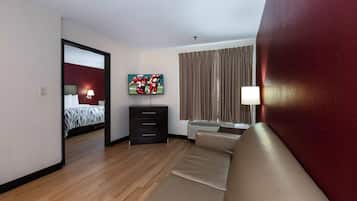 Una habitación de hotel con cama, televisor, sofá, cómoda y ventana con cortinas.