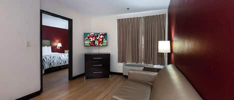 Una habitación de hotel con cama, televisor, sofá, cómoda y ventana con cortinas.
