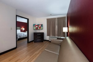 Una habitación de hotel con cama, televisor, sofá, cómoda y ventana con cortinas.