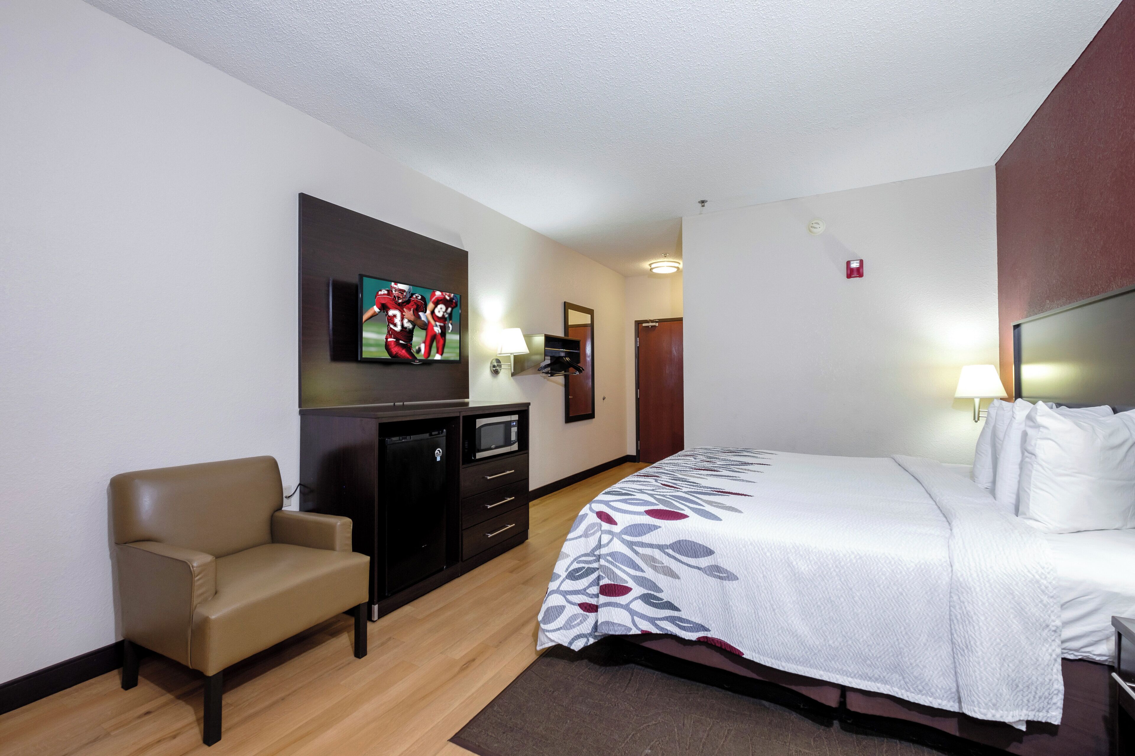 A hotel room with a bed, a desk, a chair, a television, and a door.