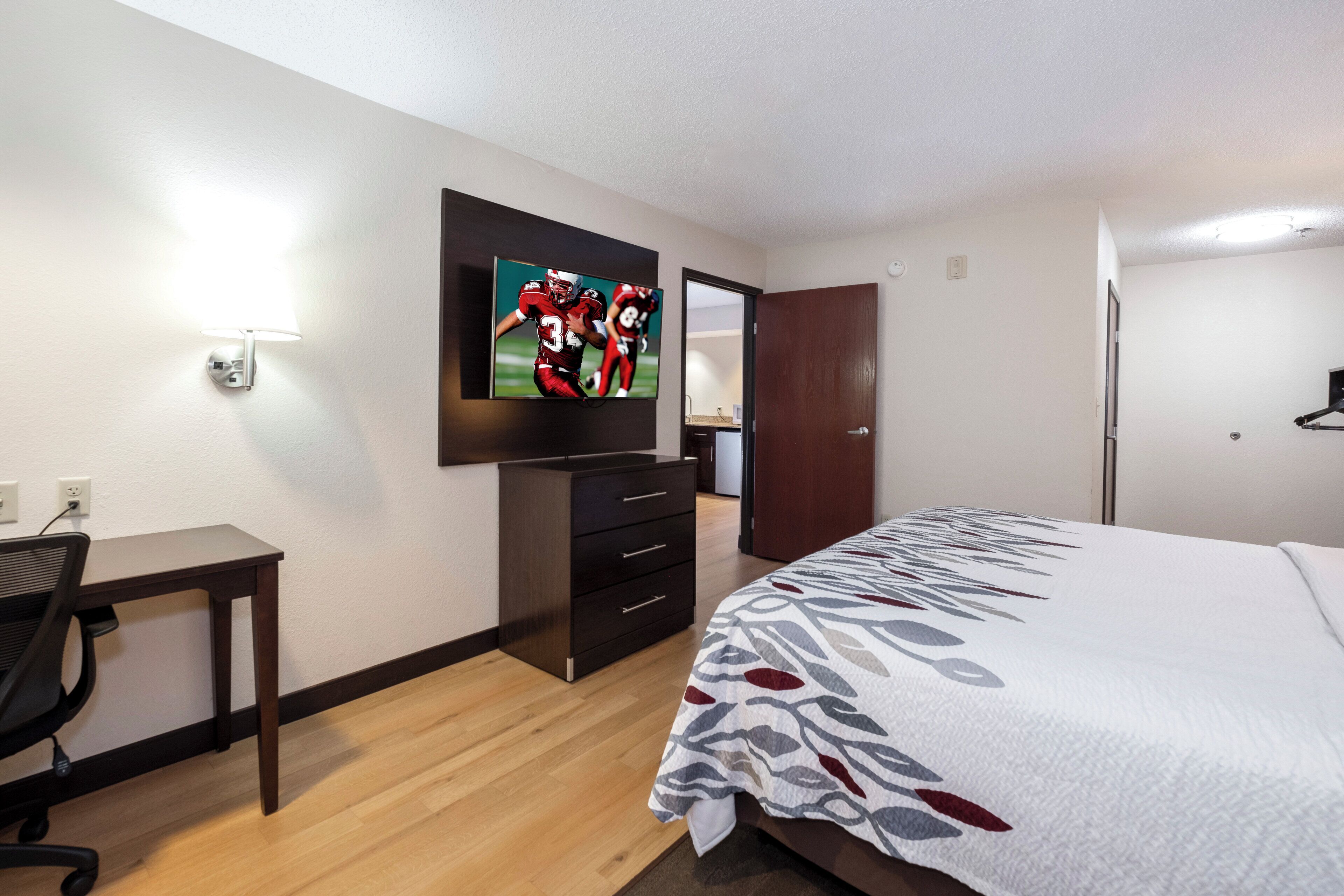 Une chambre d’hôtel comprenant un lit, un bureau, une chaise, un téléviseur fixé au mur et une armoire.