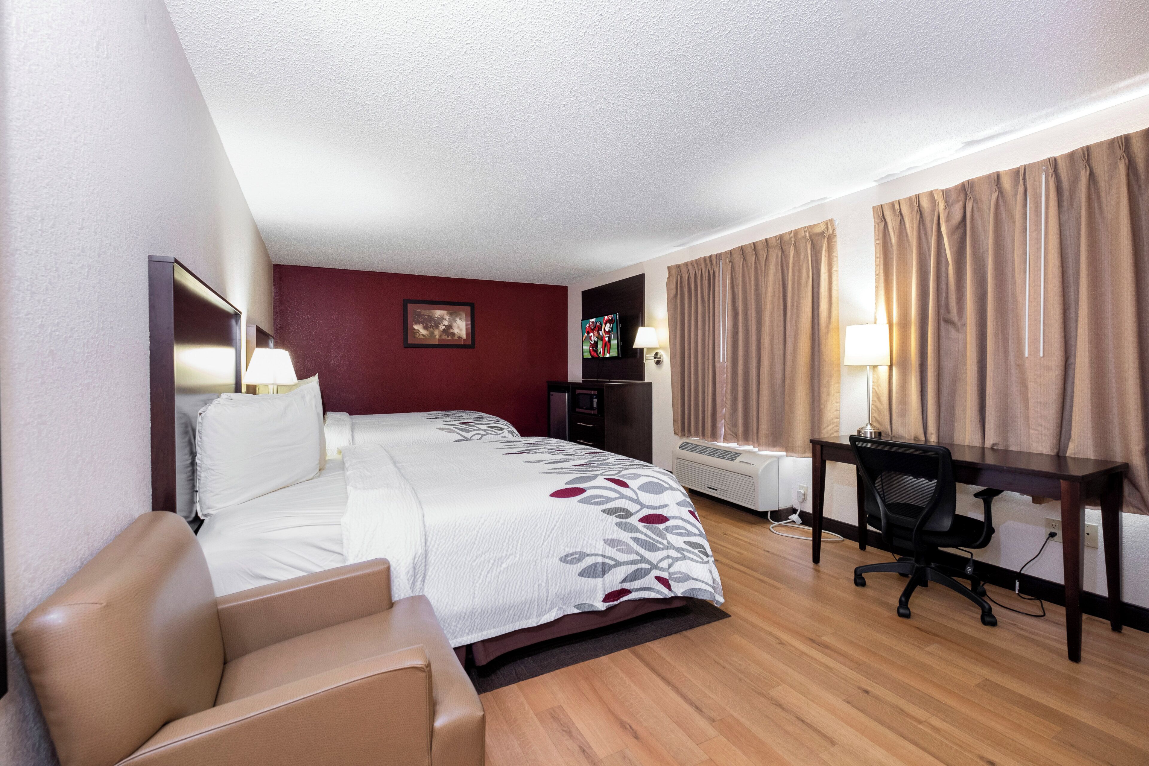 Habitación de hotel con cama, escritorio, silla, televisor y ventana con cortinas.