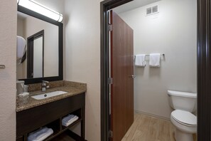 A bathroom with a granite countertop sink, a mirror, a toilet, and a wooden door. - Red Roof Inn & Suites Dover Downtown (Dover)