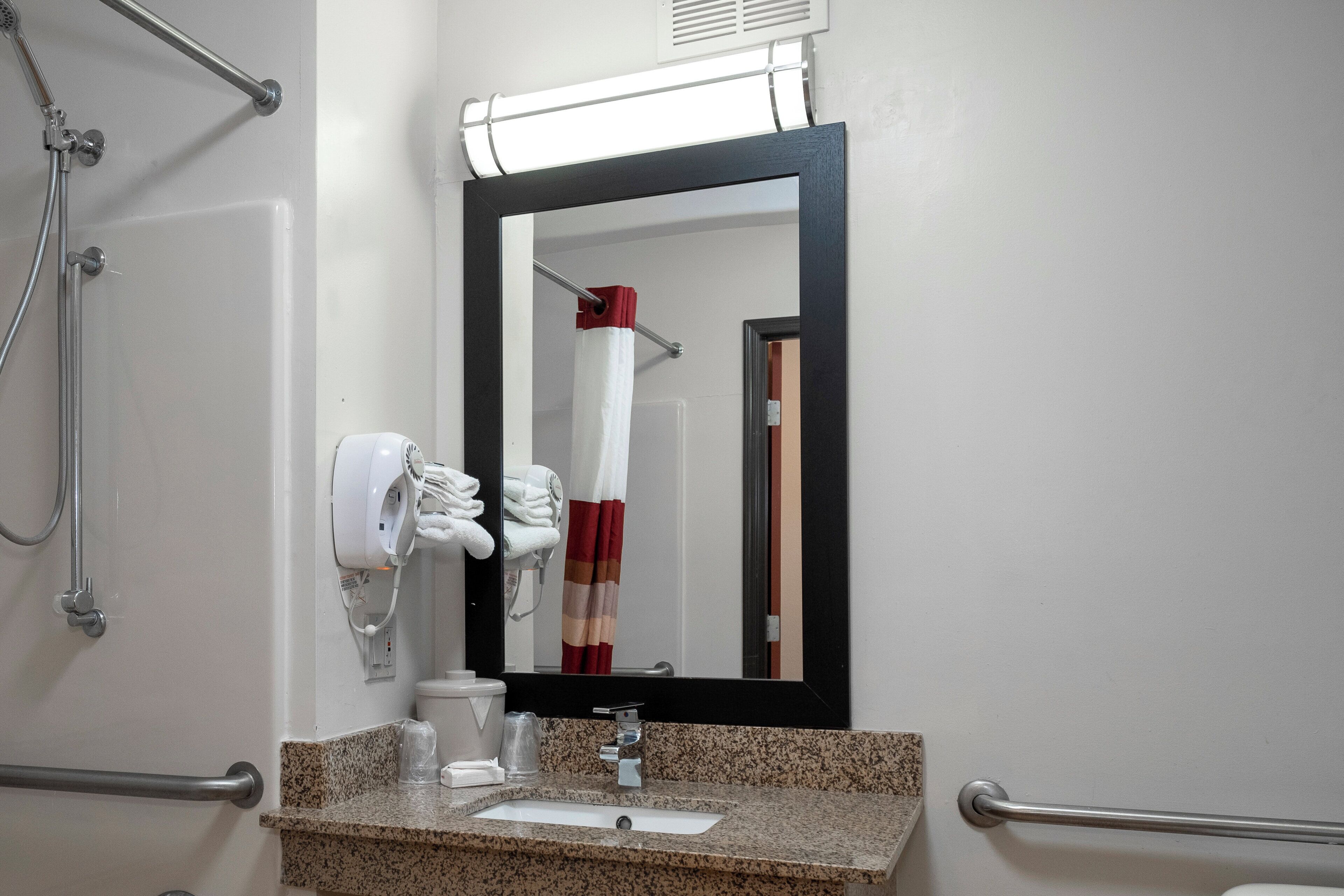 Une salle de bain équipée d’un lavabo, d’un miroir, d’un distributeur de serviettes et des commandes de la douche.