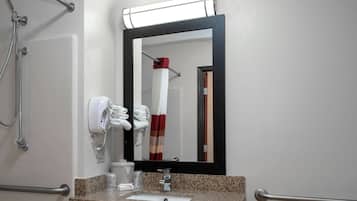 Une salle de bain équipée d’un lavabo, d’un miroir, d’un distributeur de serviettes et des commandes de la douche.