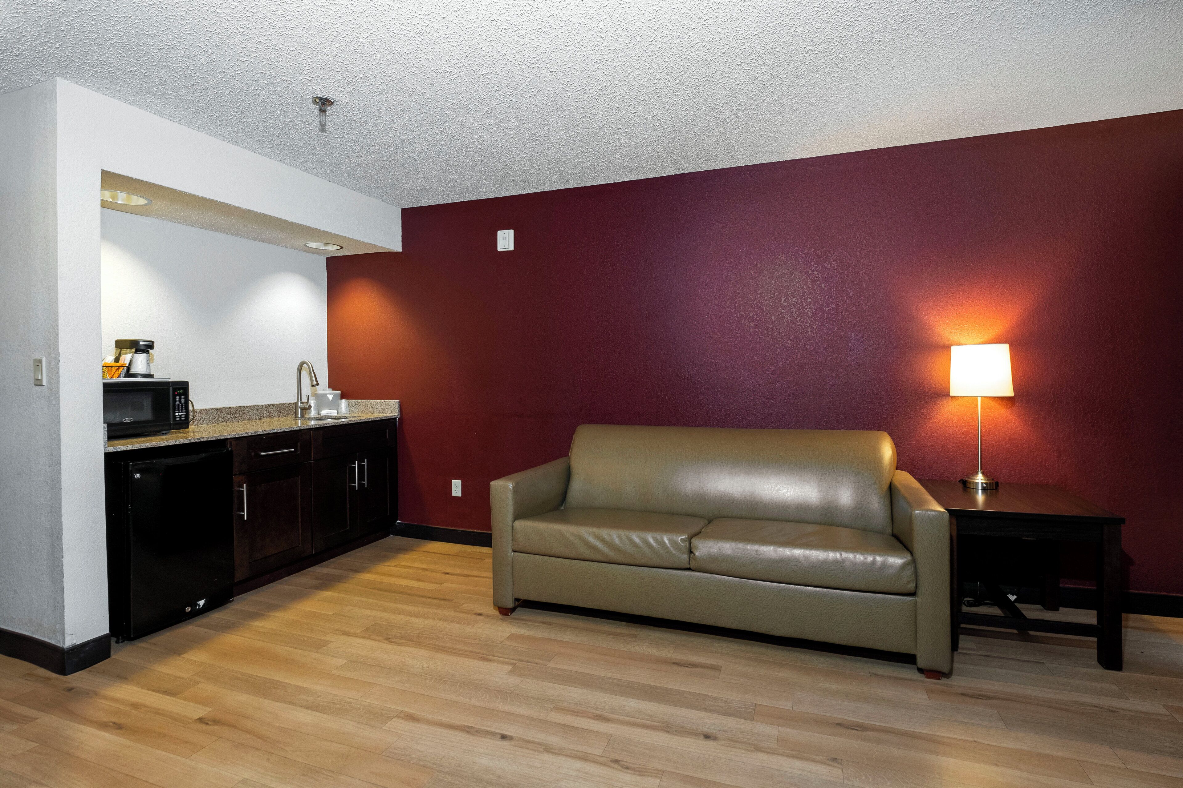 A compact living space with a kitchenette, a leather sofa, and a lamp.