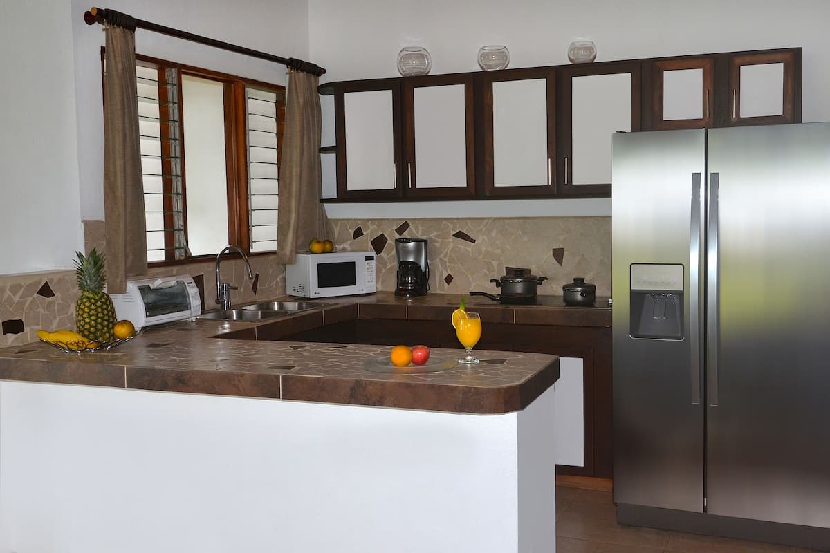 A kitchen with a refrigerator, microwave, coffee maker, and a fruit bowl.