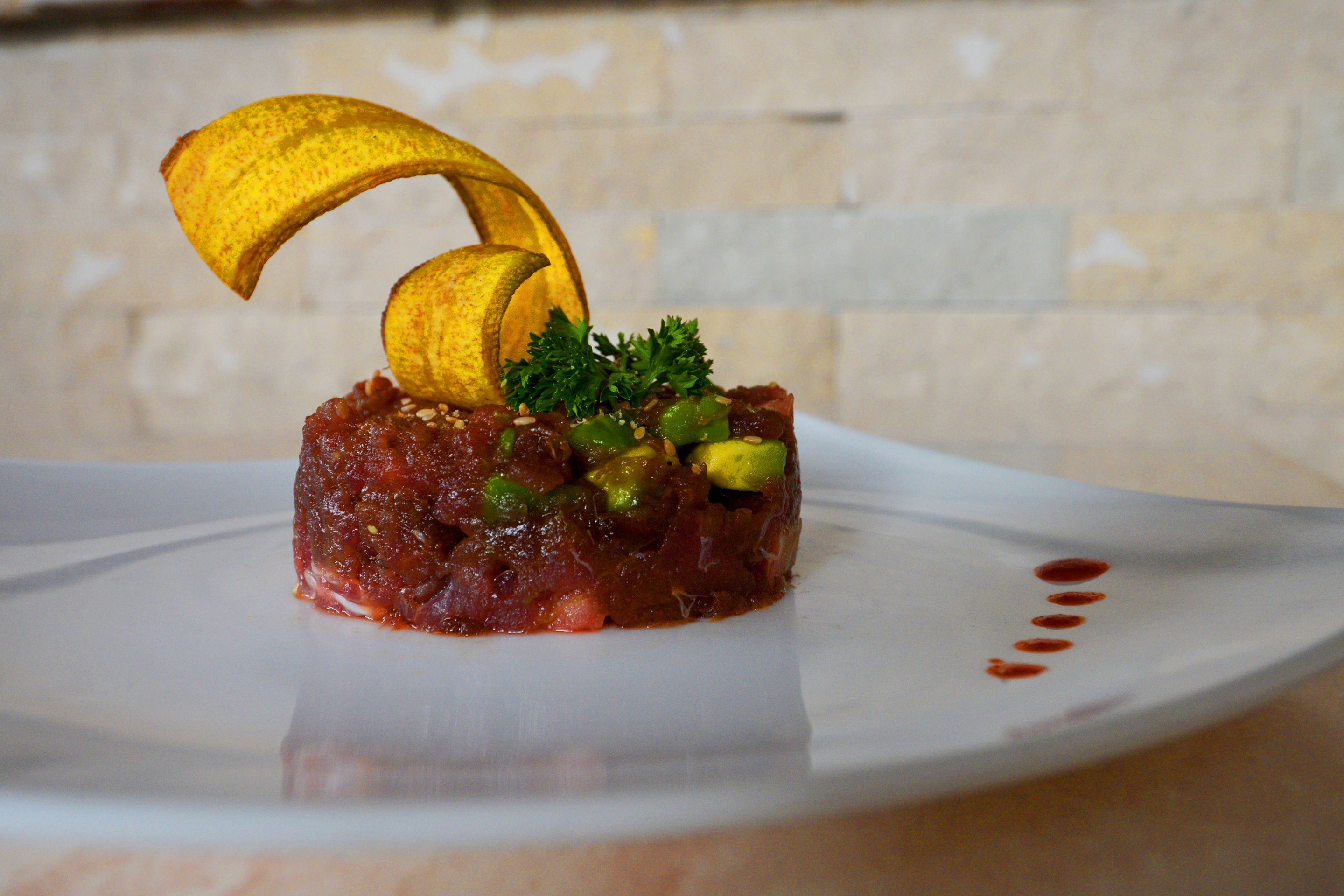 A dish with a banana slice on top, garnished with parsley and avocado, served on a white plate.