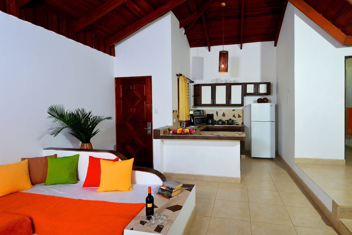 A compact living space with a kitchenette, a dining area with a sofa and cushions, and a small kitchen island.