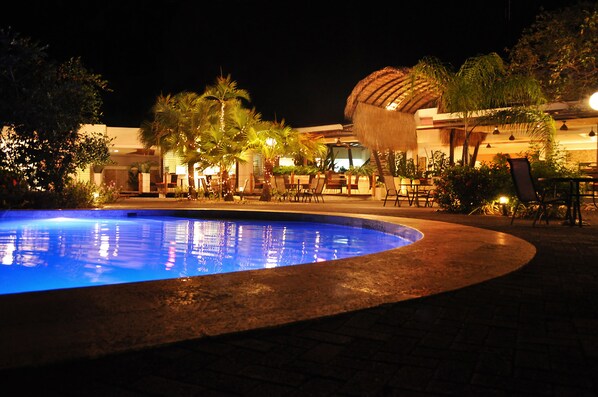 A nighttime pool area with a curved edge, palm trees, and outdoor seating.