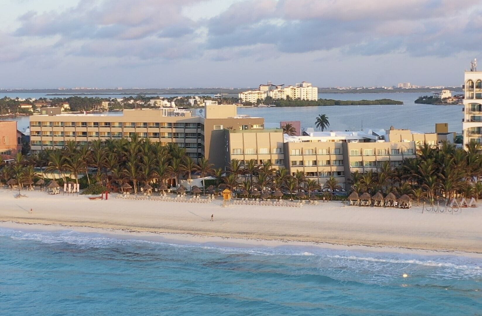 A beachfront hotel with multiple buildings, palm trees, and a sandy beach.
