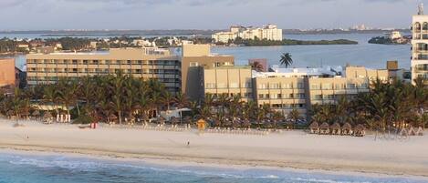 A beachfront hotel with multiple buildings, palm trees, and a sandy beach.