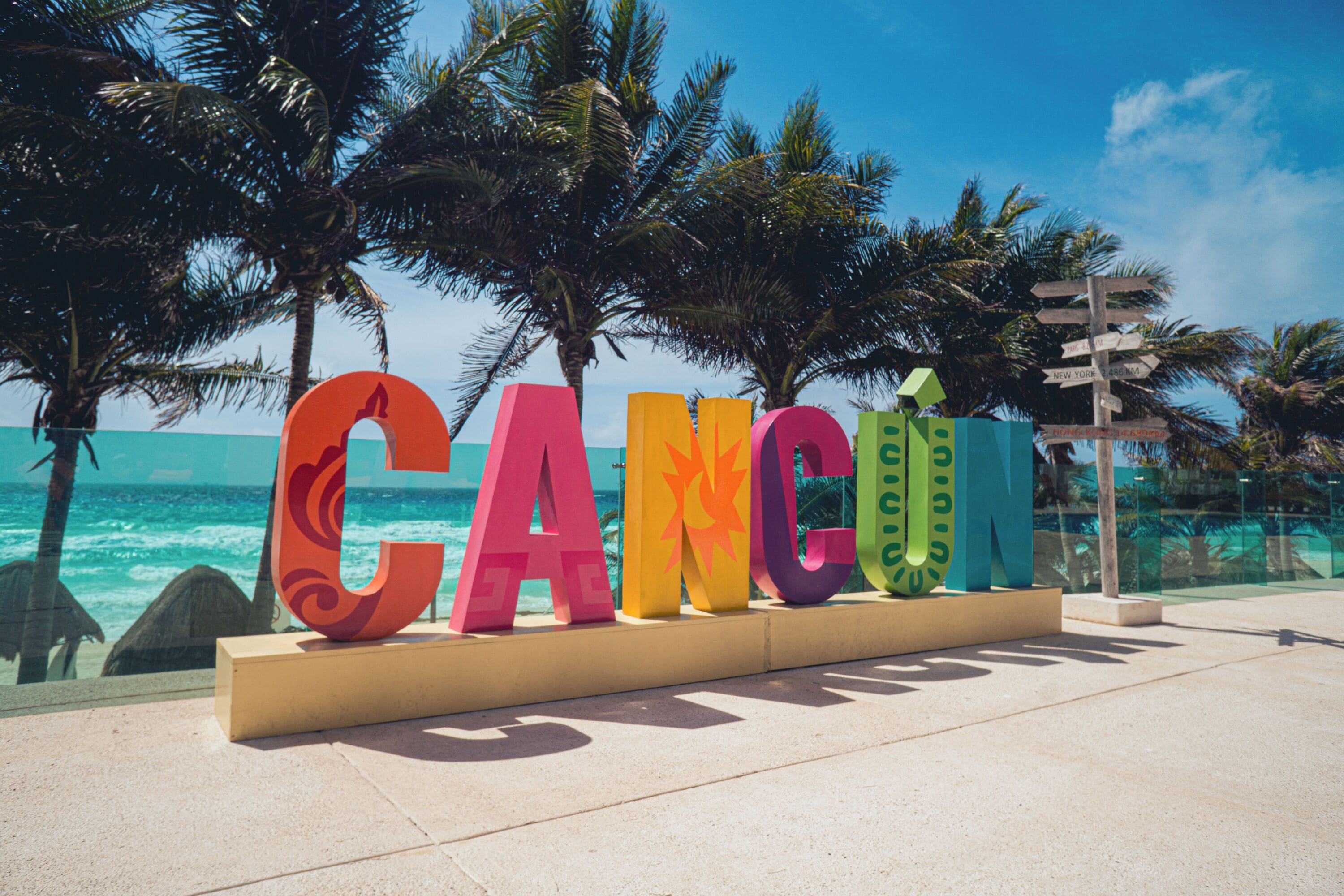 A colorful sign spelling 'CANCUN' with a palm tree and ocean in the background.