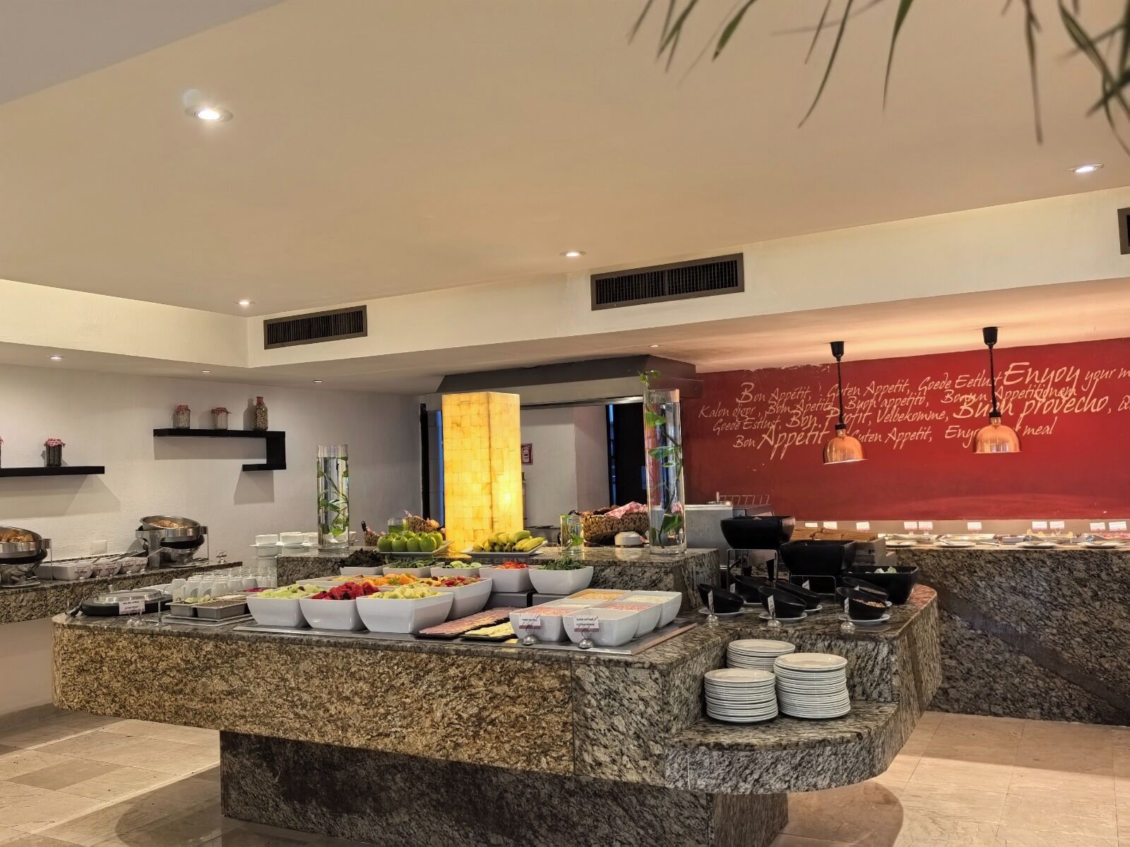 A modern kitchen with a marble countertop, various food items, and a red wall with text.
