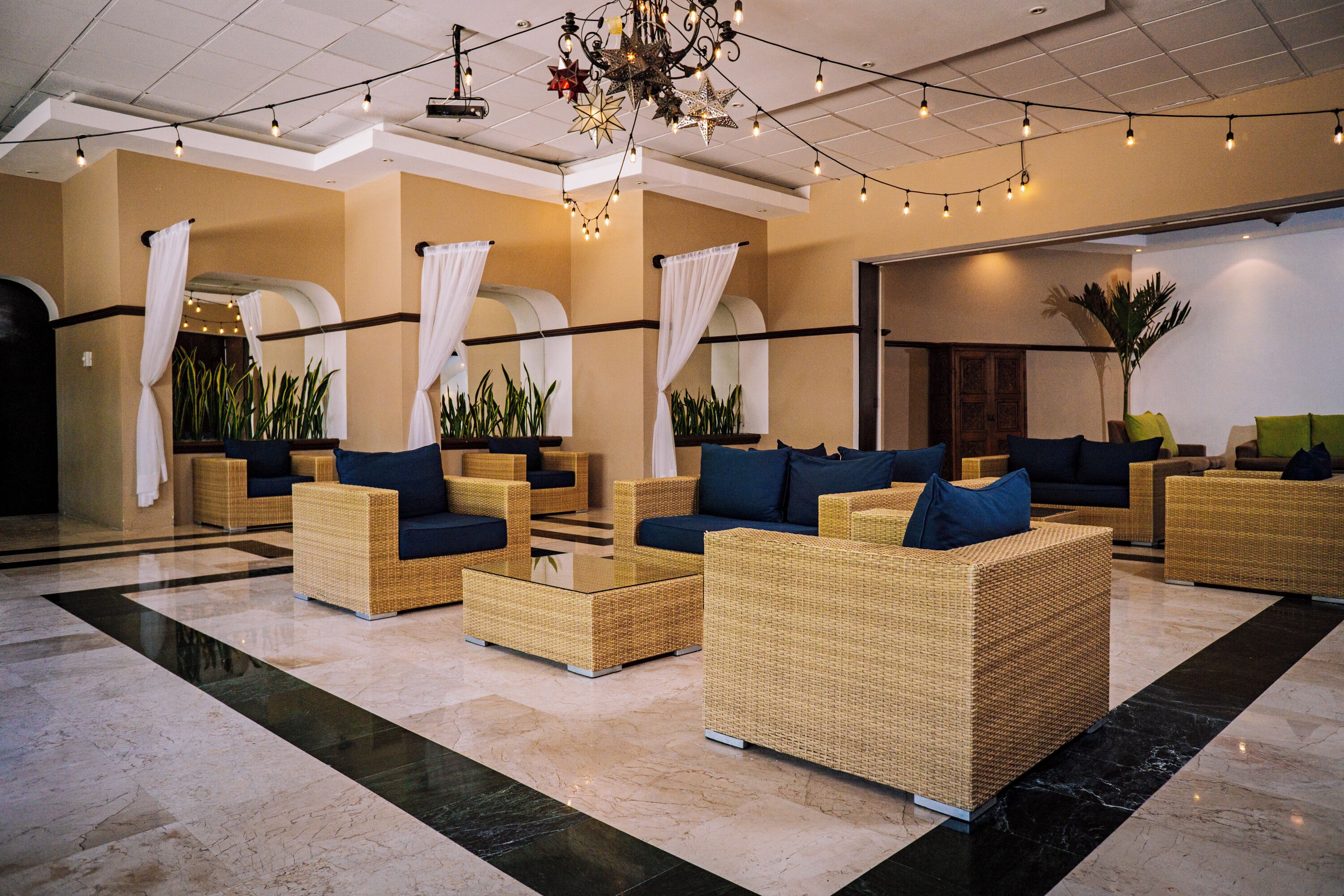 A lobby with wicker furniture, a chandelier, and potted plants.