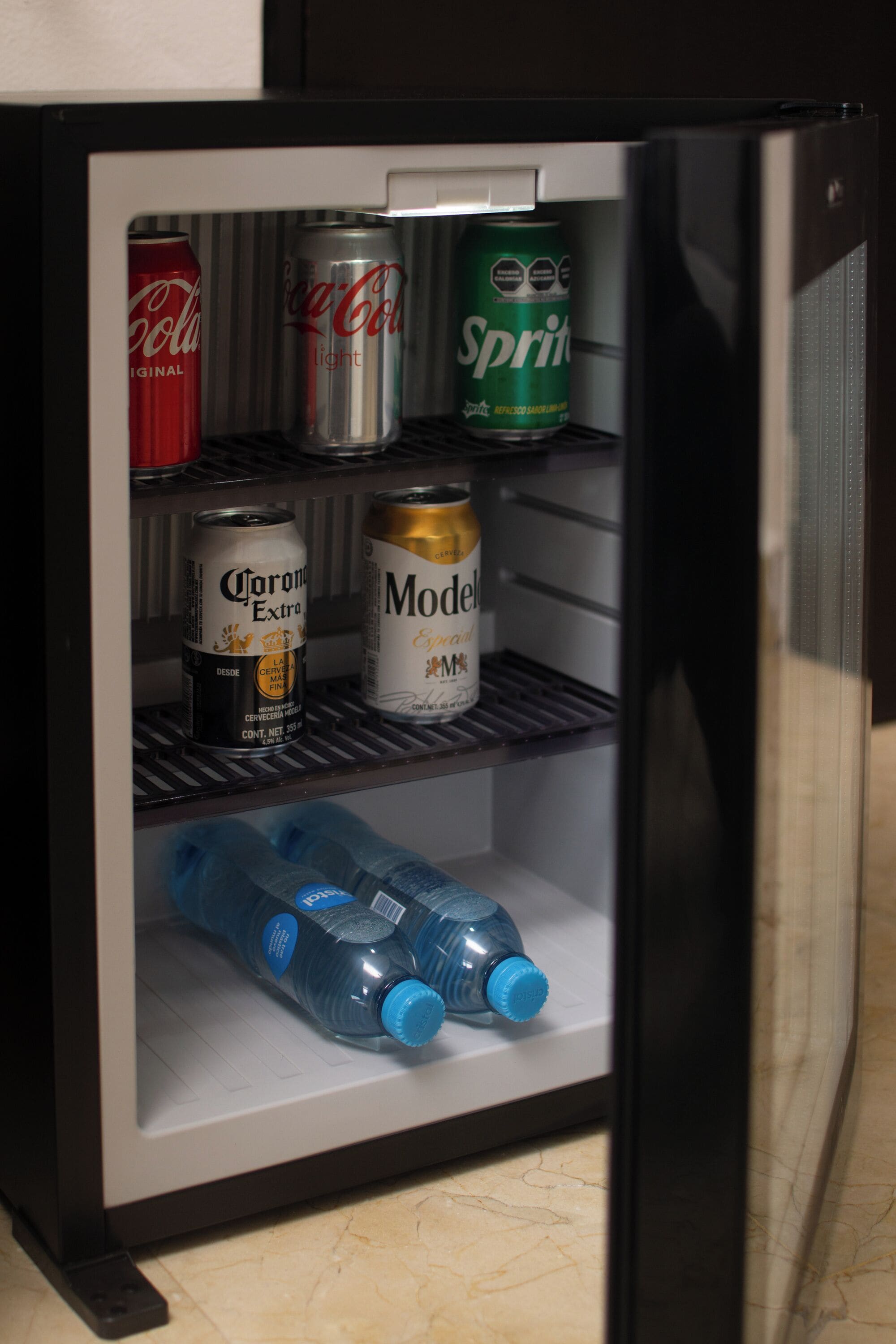 Een minibar met drankjes, waaronder Corona Extra, Modelo, Sprite en twee blauwe waterflessen.