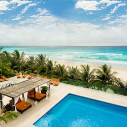 Relax by the oceanfront pool surrounded by palm trees and a shaded pergola.