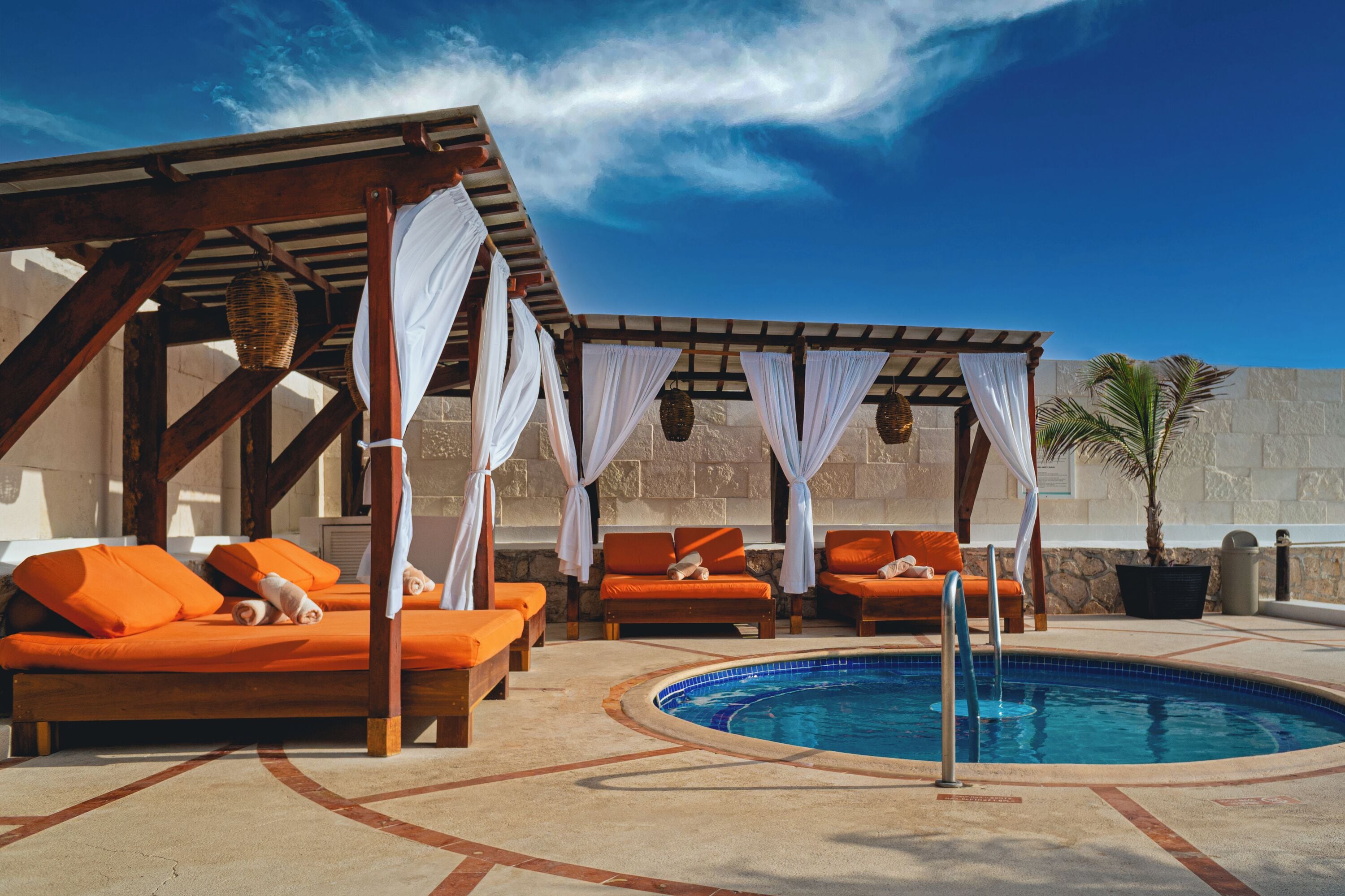 A poolside area with lounge chairs, a pool, and a pergola with white curtains.