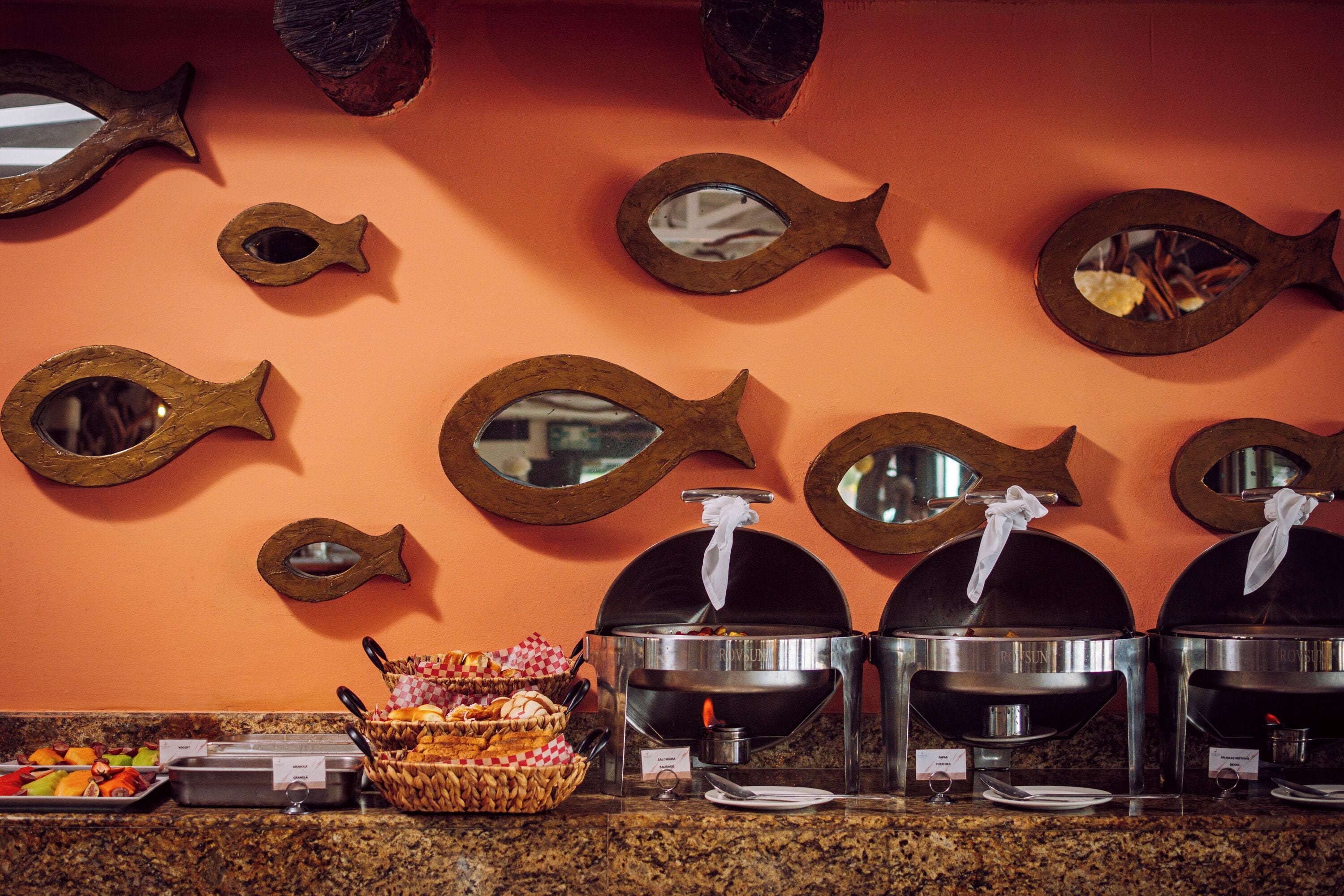 Un buffet avec plusieurs points de service, une grande variété de plats et des miroirs décoratifs en forme de poisson accrochés au mur.