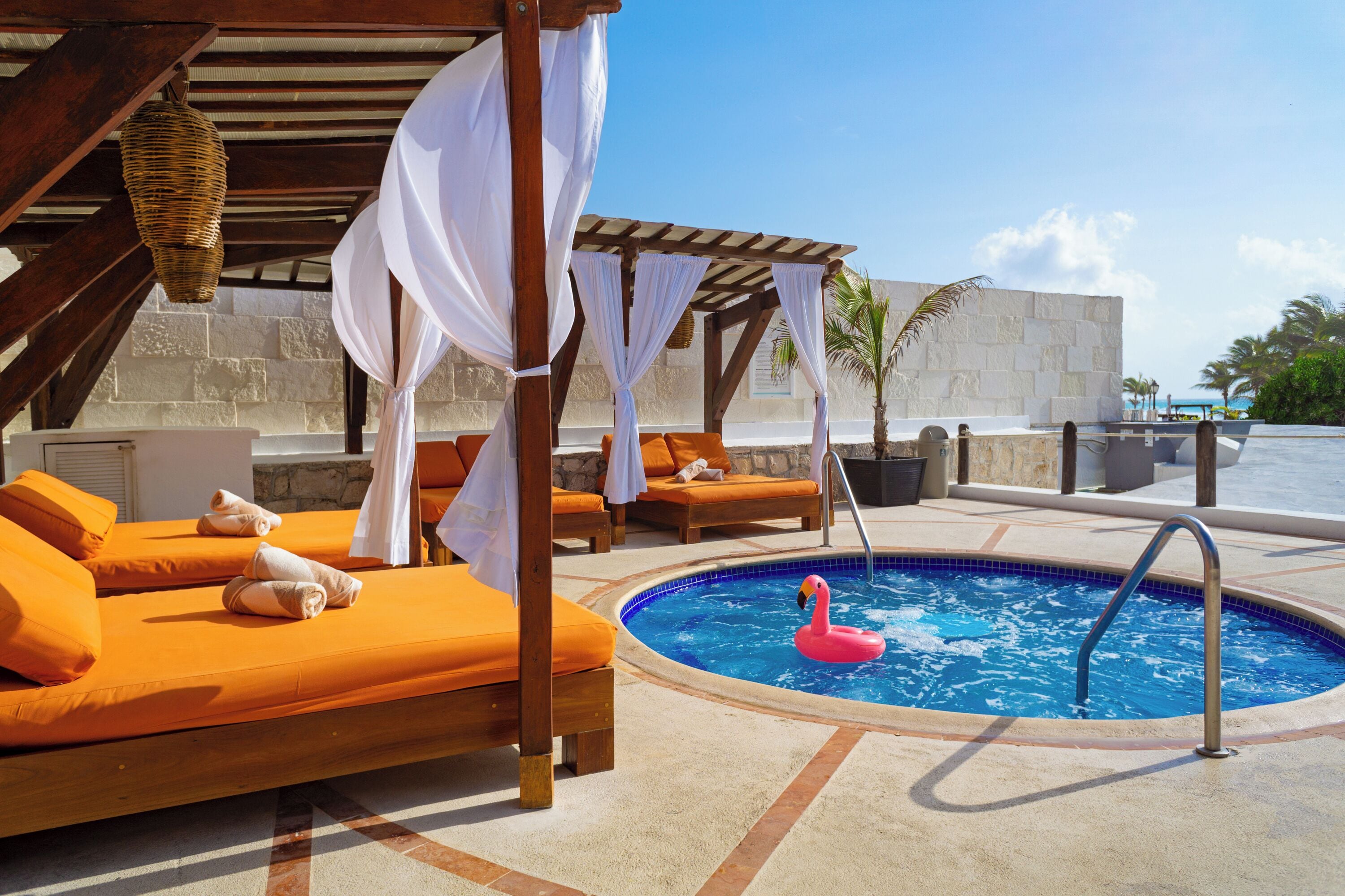 A poolside area with lounge chairs, a pool with a flamingo float, and a pergola with white drapes.