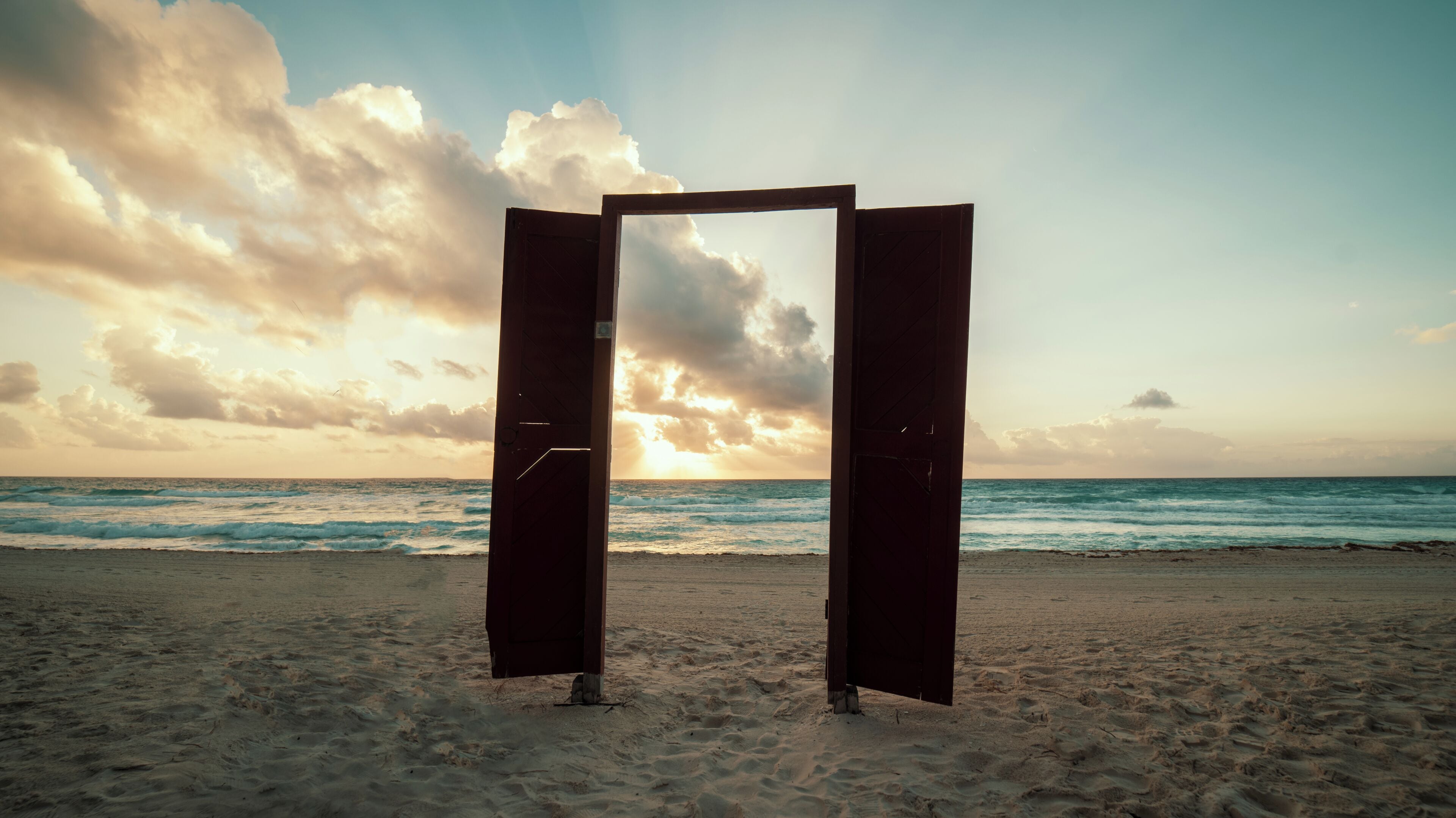 An open doorway on a beach with the ocean and sky in the background.