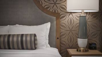 A neatly made bed with white linens and a patterned pillow, a bedside lamp, and a digital clock on a wooden bedside table.